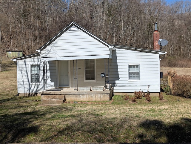 view of front facade featuring a front yard, a forest view, and covered porch