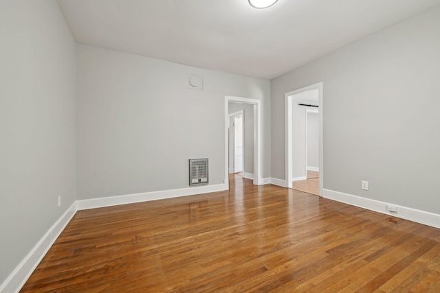 spare room featuring heating unit, baseboards, and wood-type flooring