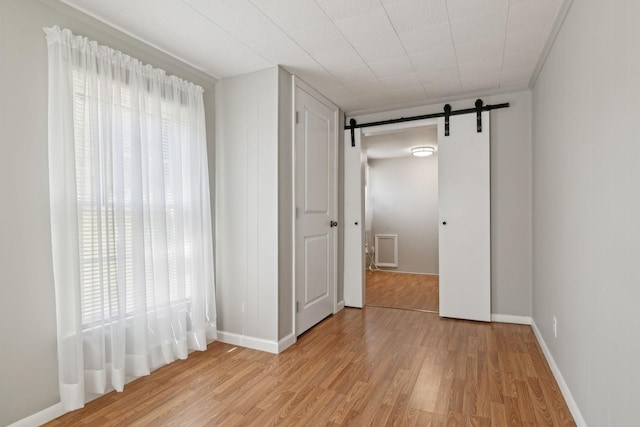 unfurnished room featuring a barn door, baseboards, and light wood finished floors