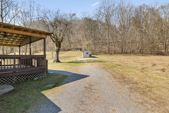 view of yard featuring an outbuilding, driveway, a wooden deck, and a storage shed