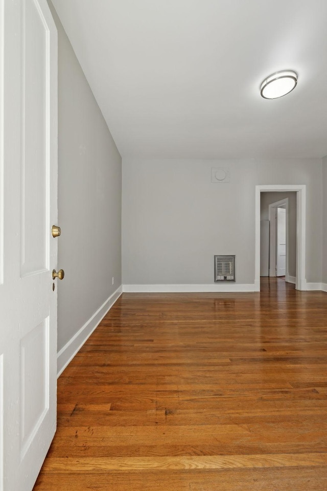 unfurnished room featuring heating unit, wood finished floors, and baseboards