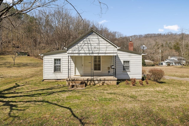 view of front of house with a chimney, covered porch, and a front yard