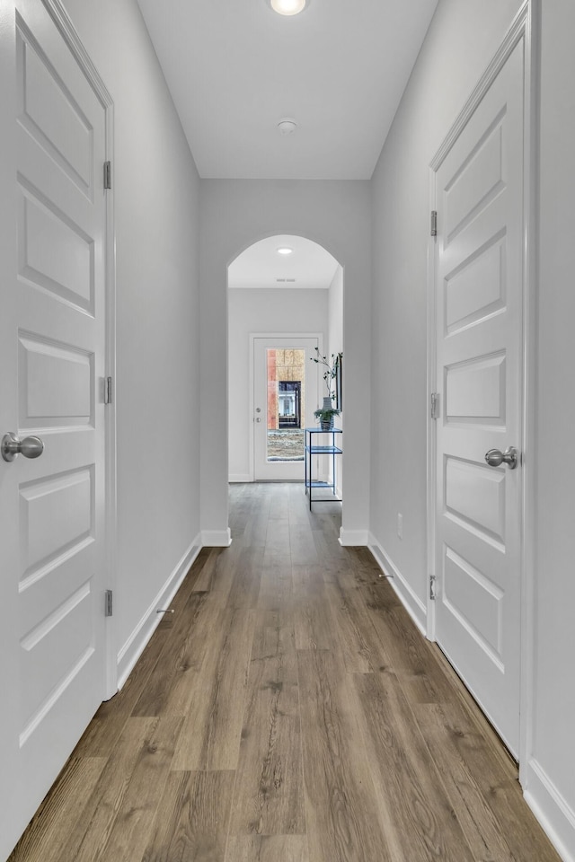 hallway with baseboards, arched walkways, and dark wood-style floors