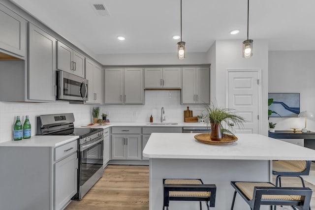 kitchen with gray cabinets, a kitchen breakfast bar, stainless steel appliances, and a sink