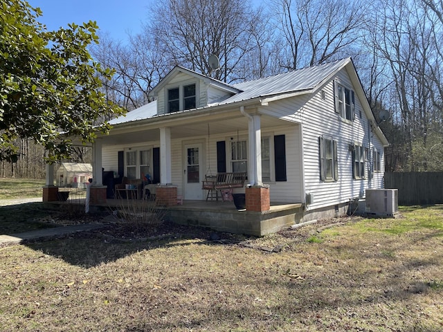 bungalow with a front lawn, fence, covered porch, metal roof, and central AC unit