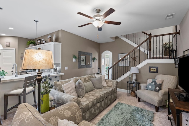 living room with visible vents, stairs, light carpet, arched walkways, and a ceiling fan