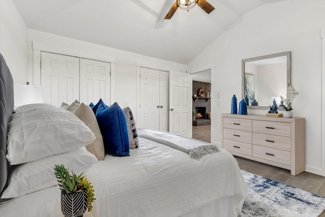 bedroom featuring a brick fireplace, multiple closets, lofted ceiling, wood finished floors, and a ceiling fan