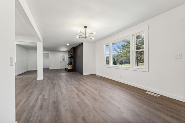 unfurnished living room featuring a notable chandelier, visible vents, baseboards, and wood finished floors