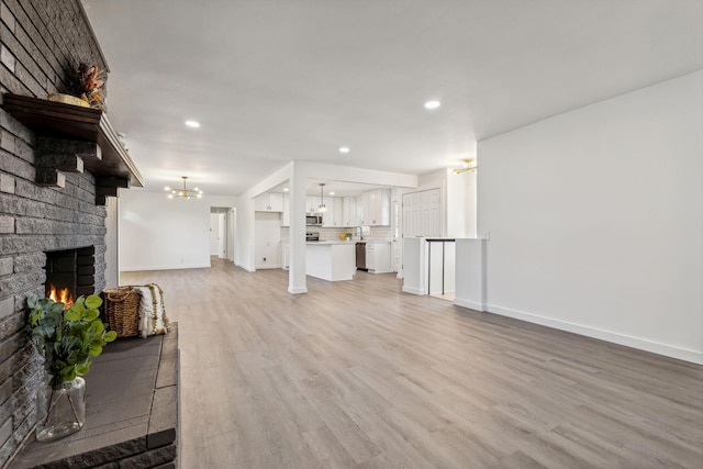 unfurnished living room featuring baseboards, recessed lighting, a brick fireplace, a notable chandelier, and light wood-type flooring