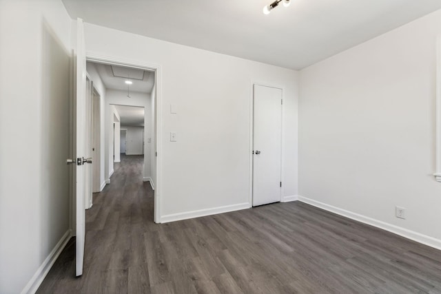 unfurnished bedroom featuring dark wood-style floors, attic access, and baseboards