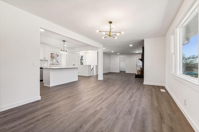 unfurnished living room with baseboards, a notable chandelier, and wood finished floors