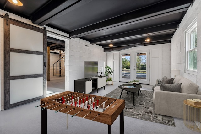 playroom with a barn door, concrete block wall, french doors, and beam ceiling