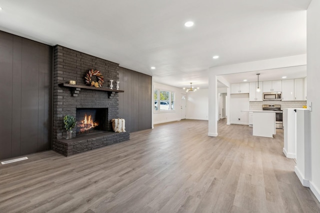 unfurnished living room with light wood-type flooring, visible vents, recessed lighting, a fireplace, and a chandelier