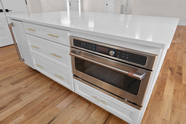 interior details featuring oven, light wood-type flooring, light countertops, and white cabinetry