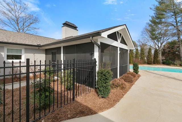 view of property exterior featuring fence, a fenced in pool, a sunroom, a shingled roof, and a chimney