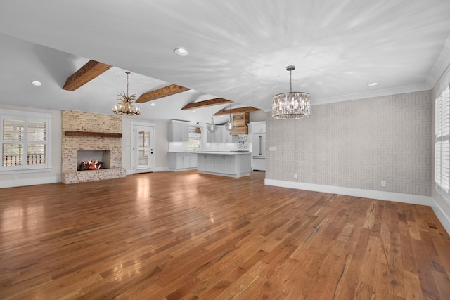 unfurnished living room with baseboards, wallpapered walls, an inviting chandelier, beam ceiling, and a brick fireplace