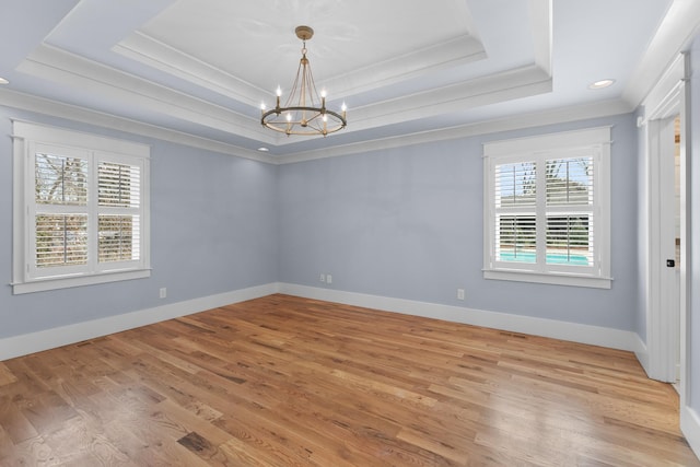 spare room featuring a raised ceiling, a notable chandelier, light wood-style flooring, crown molding, and baseboards