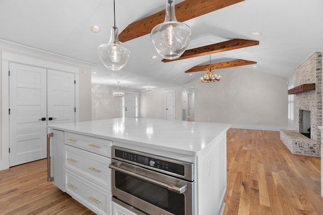 kitchen with open floor plan, white cabinetry, a brick fireplace, and vaulted ceiling with beams