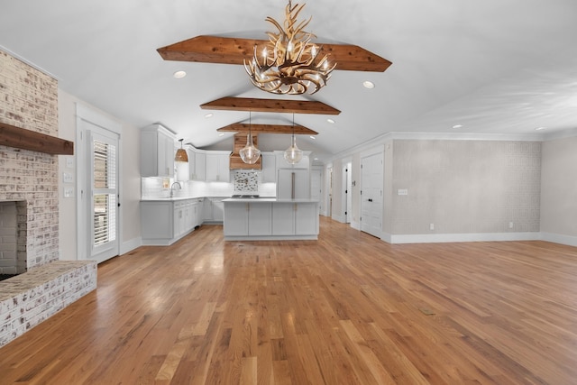 kitchen with light wood-style flooring, a sink, lofted ceiling with beams, a fireplace, and light countertops