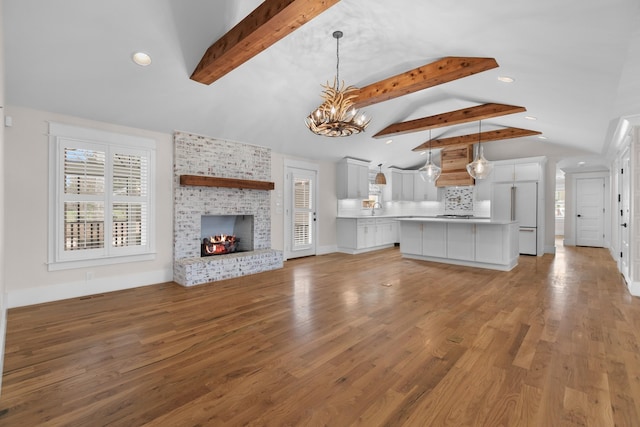 unfurnished living room featuring a notable chandelier, a sink, light wood-style floors, a fireplace, and vaulted ceiling with beams