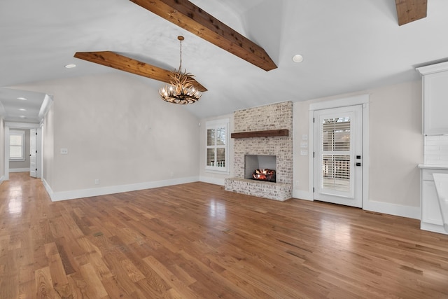 unfurnished living room featuring light wood-style flooring, lofted ceiling with beams, baseboards, a brick fireplace, and a chandelier