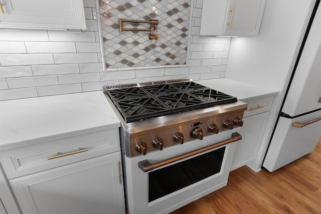 kitchen with high end range, light wood finished floors, freestanding refrigerator, decorative backsplash, and white cabinets