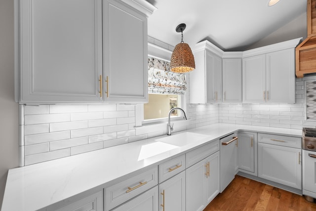 kitchen featuring a sink, decorative backsplash, light countertops, vaulted ceiling, and stainless steel dishwasher