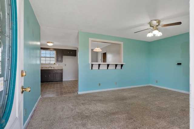 carpeted spare room with a ceiling fan, baseboards, and a sink