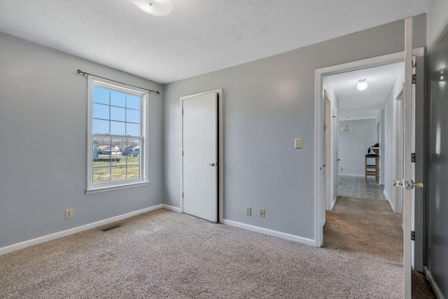 unfurnished bedroom featuring visible vents, a textured ceiling, baseboards, and carpet floors