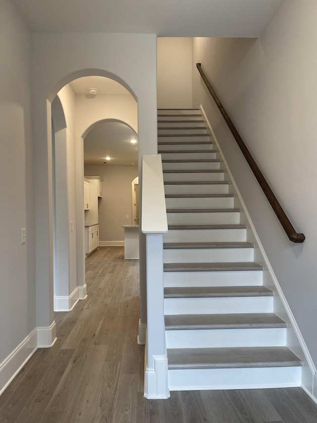 stairs featuring wood finished floors, baseboards, and arched walkways