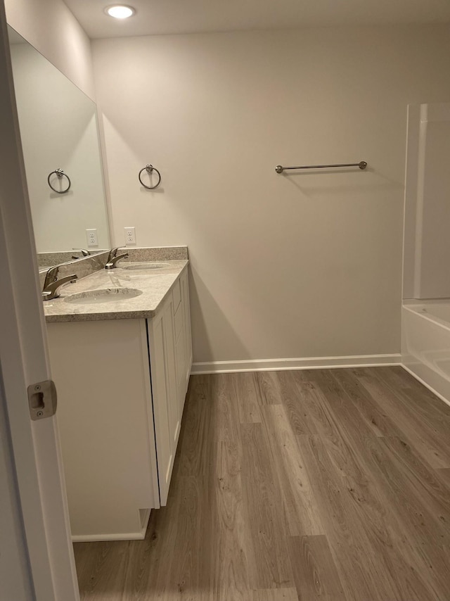 full bathroom featuring a sink, wood finished floors, double vanity, baseboards, and a bathtub