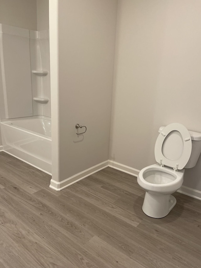 full bath featuring baseboards, toilet, wood finished floors, and bathing tub / shower combination