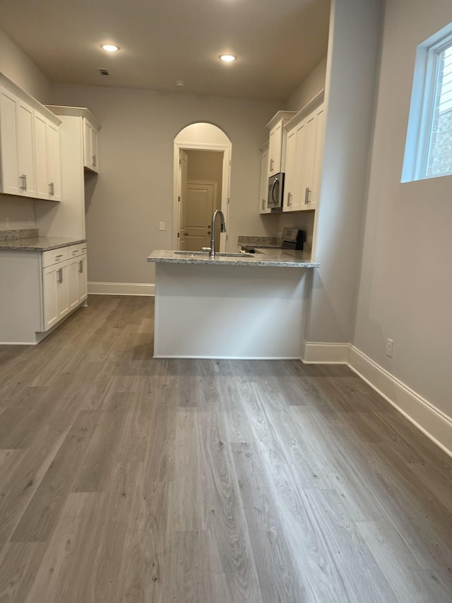 kitchen featuring a sink, stainless steel microwave, white cabinetry, arched walkways, and a peninsula