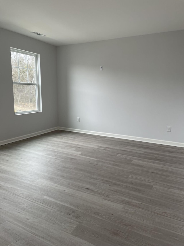 unfurnished room featuring dark wood-type flooring, visible vents, and baseboards