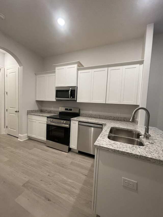 kitchen featuring light stone countertops, arched walkways, a sink, stainless steel appliances, and white cabinets