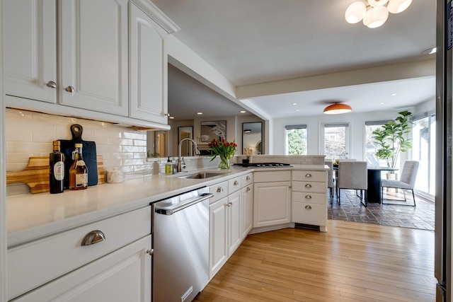 kitchen with light wood finished floors, white cabinetry, a sink, decorative backsplash, and stainless steel dishwasher