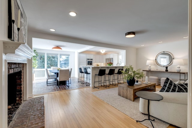 living area with recessed lighting, wood-type flooring, and a brick fireplace