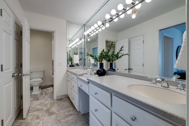 bathroom with double vanity, toilet, baseboards, and a sink