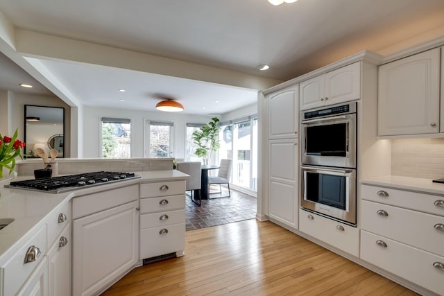 kitchen featuring light wood-type flooring, stainless steel appliances, white cabinets, light countertops, and decorative backsplash