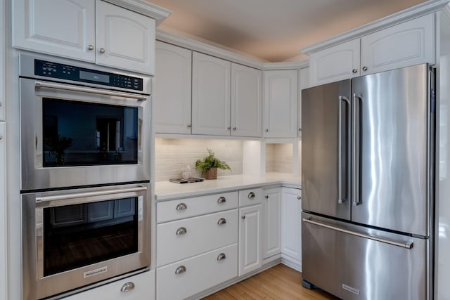 kitchen featuring decorative backsplash, white cabinets, appliances with stainless steel finishes, and light countertops