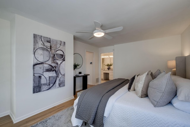 bedroom featuring wood finished floors, visible vents, baseboards, ensuite bath, and ceiling fan