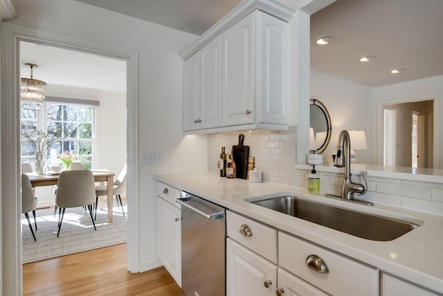 kitchen with light wood-type flooring, a sink, stainless steel dishwasher, backsplash, and white cabinets