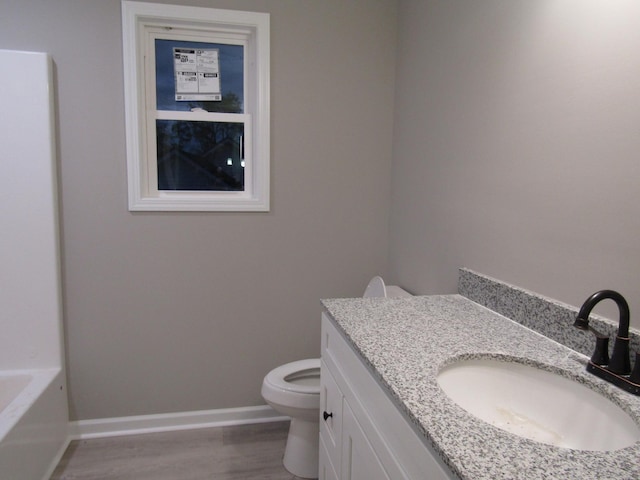 full bathroom with vanity, wood finished floors, baseboards, toilet, and a washtub