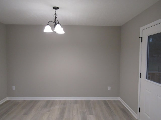 empty room with baseboards, an inviting chandelier, and light wood-style flooring