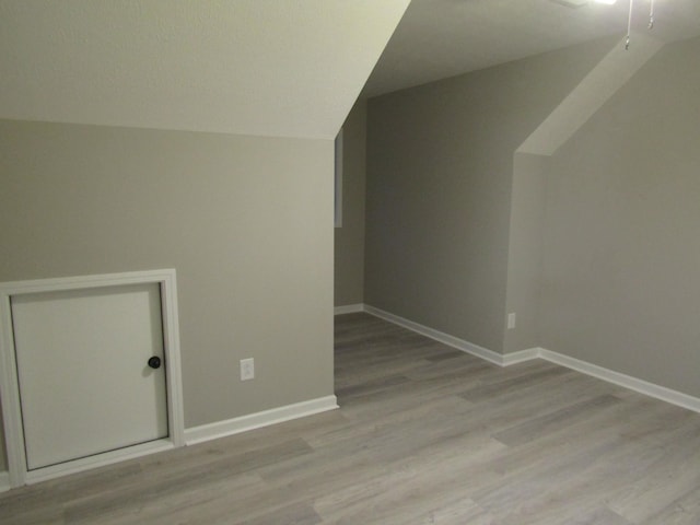 additional living space with light wood-style flooring, baseboards, and vaulted ceiling