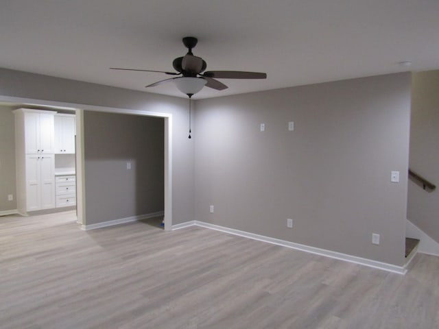 empty room featuring light wood-style flooring, a ceiling fan, stairs, and baseboards