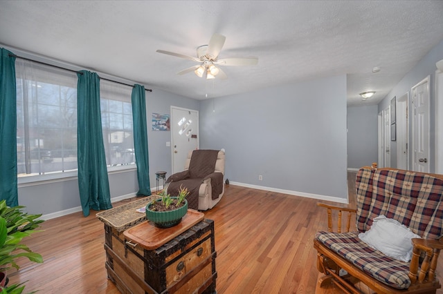 living room with light wood-style flooring, a ceiling fan, and baseboards