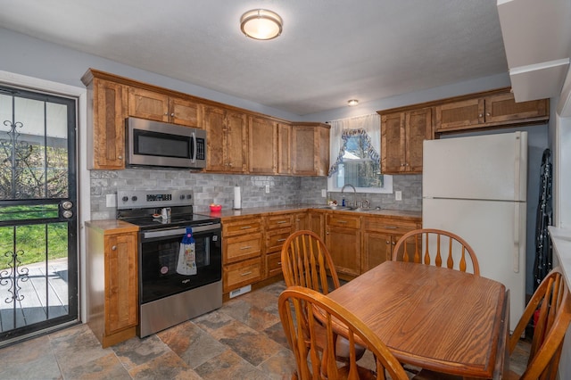 kitchen featuring brown cabinetry, decorative backsplash, stainless steel appliances, and a sink