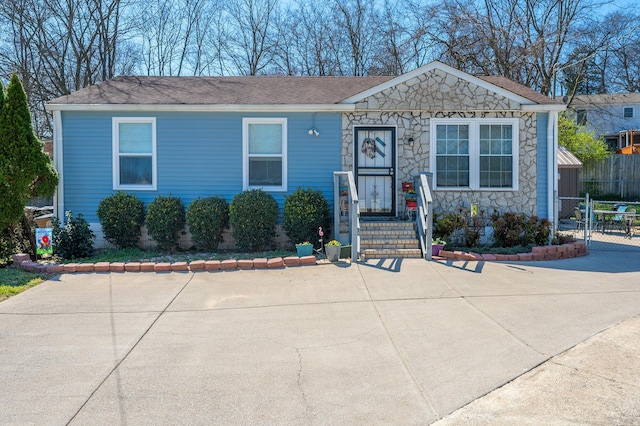 view of front of house featuring stone siding, roof with shingles, and fence