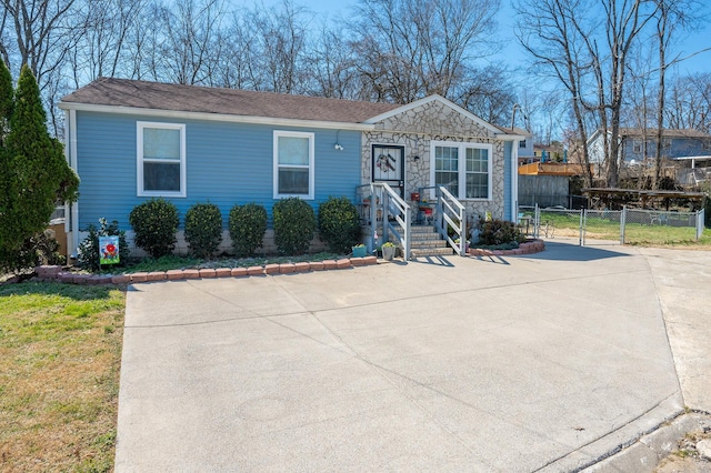 view of front facade with stone siding, concrete driveway, and fence